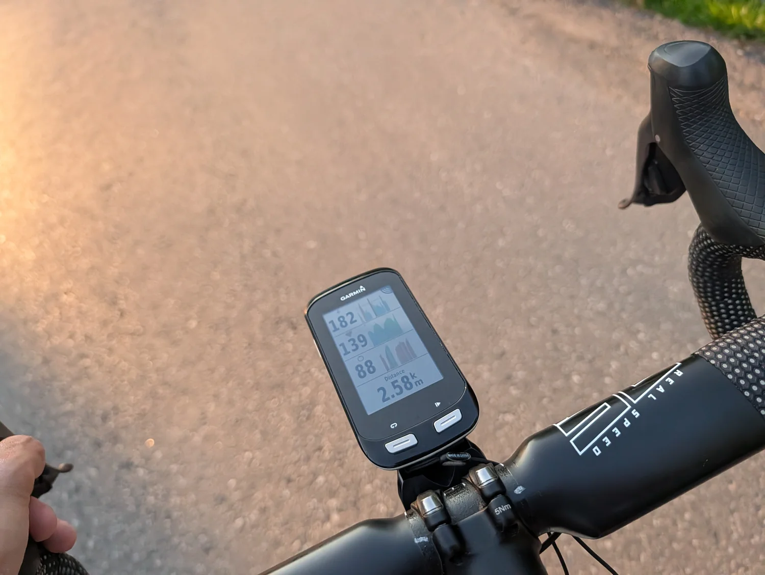 The resurrected Garmin Edge 1000 mounted on the handlebars at golden hour, running the custom-built ConnectIQ data field that stacks power, heart rate and cadence with live sparklines, over a distance of 2.58 km