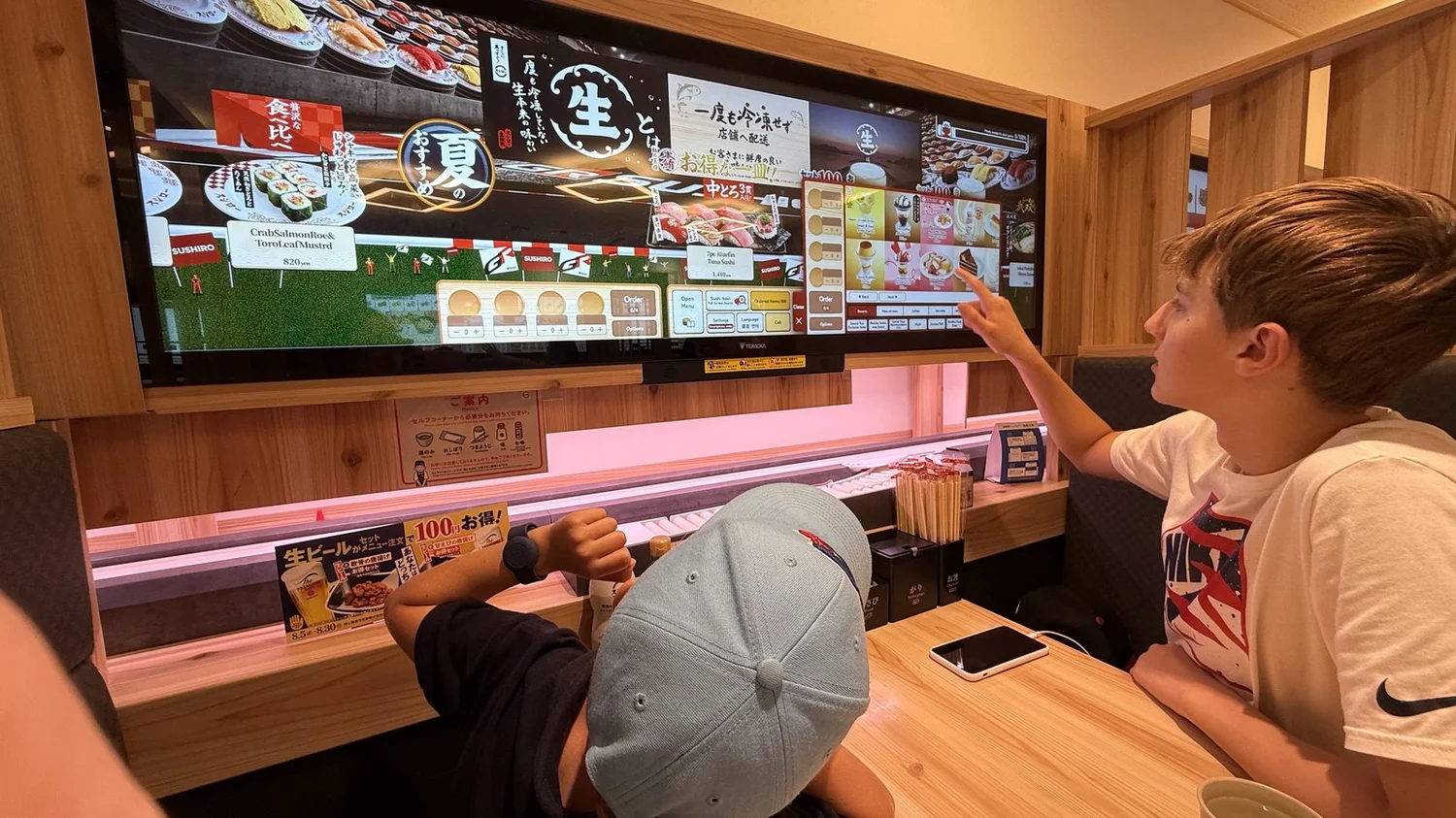A teenager tapping the order screen above the delivery lane at a Sushiro conveyor-belt sushi restaurant