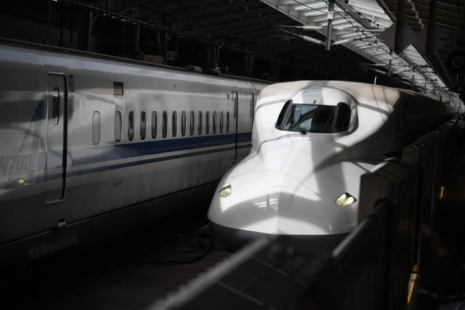 The nose of an N700 Shinkansen under a dark platform canopy