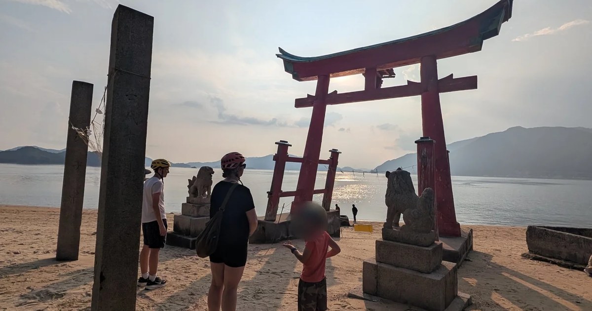 A family standing on a beach before a red torii on the Shimanami Kaido at golden hour
