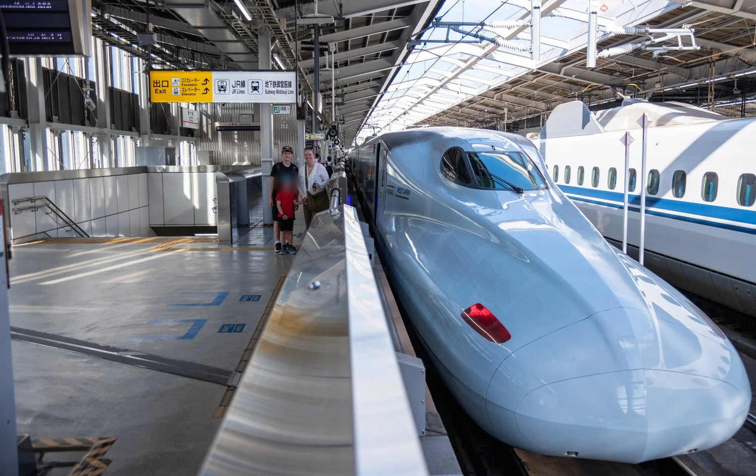 A family on a Shinkansen platform beside the nose of an N700; the youngest's face is blurred