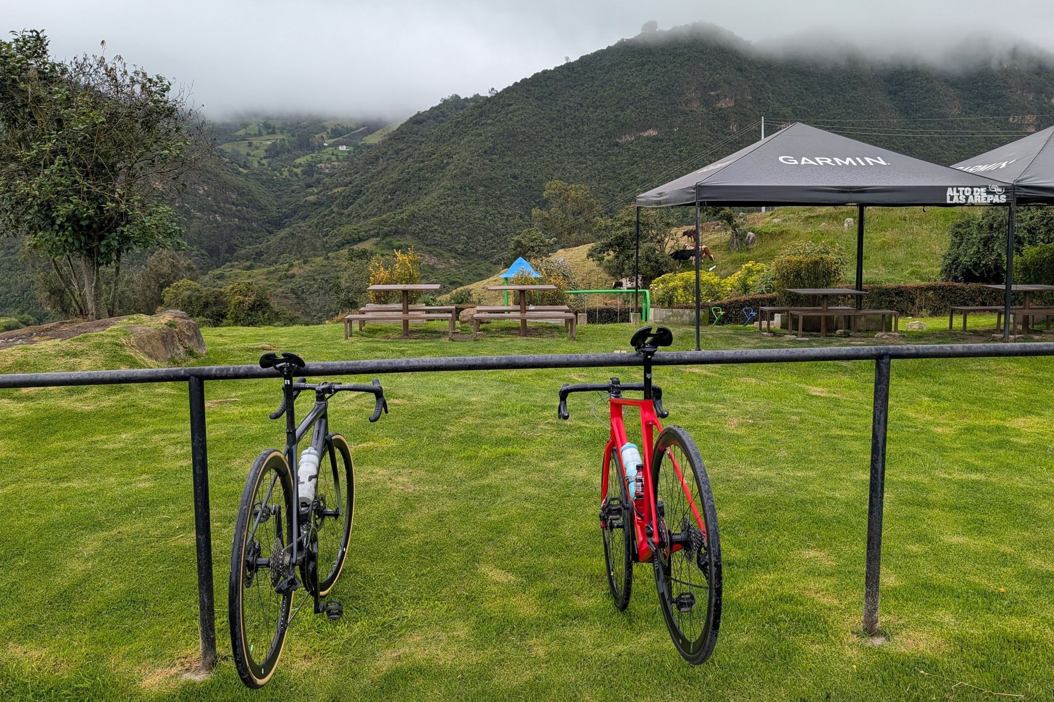 Two road bikes on a rail below misty green hills in Colombia, a Garmin tent behind them