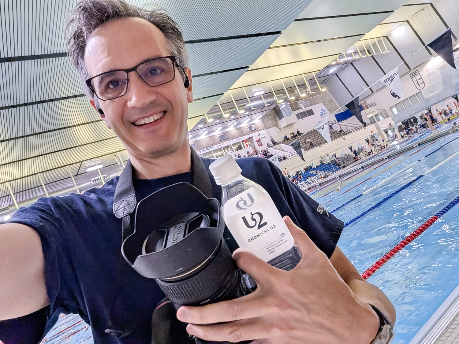 Rob taking a selfie on the pool deck, an earbud in his ear, holding his camera and a bottle of Onomichi U2 water
