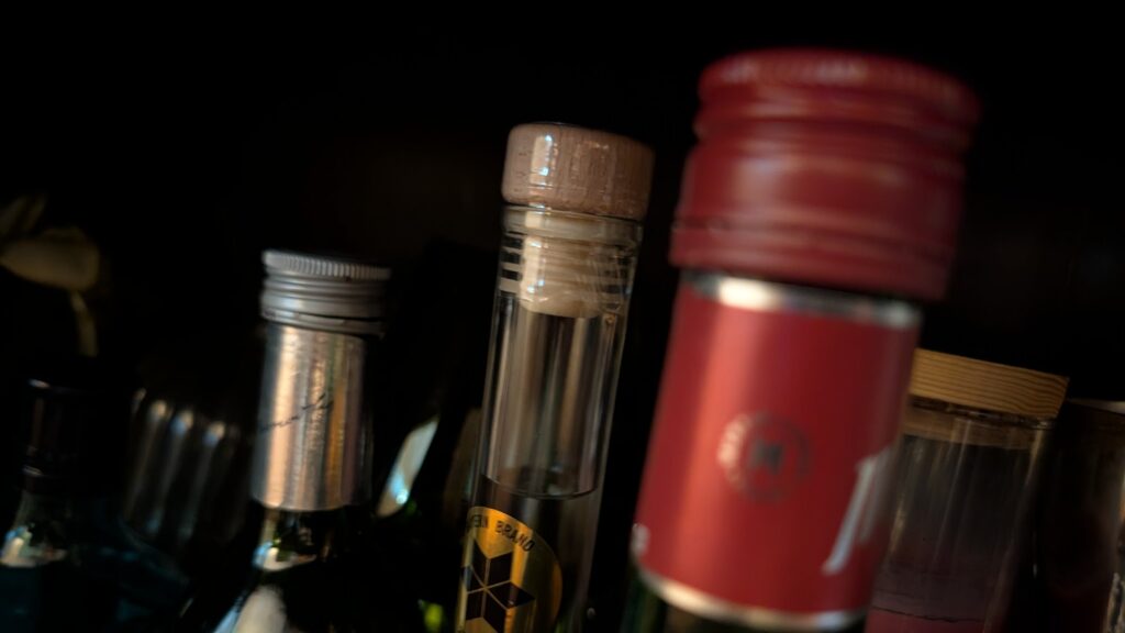Bottle tops in a dark cabinet: a cork, a red screw cap, a silver cap, nothing legible.