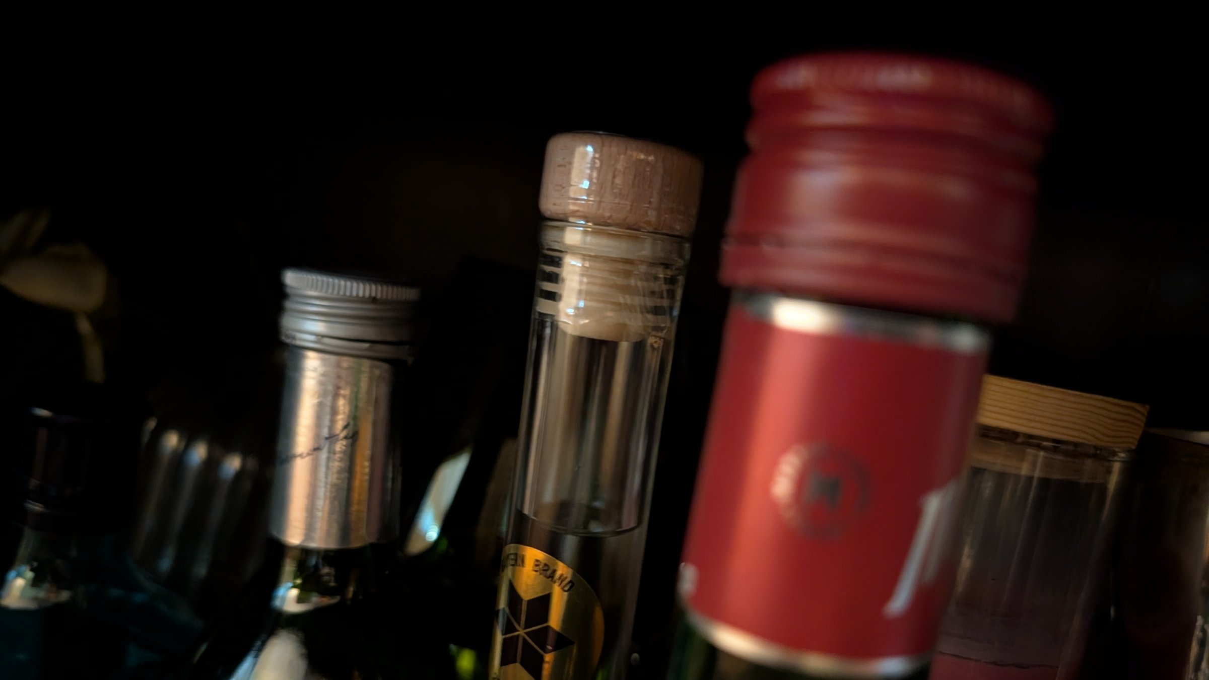 Bottle tops in a dark cabinet: a cork, a red screw cap, a silver cap, nothing legible.